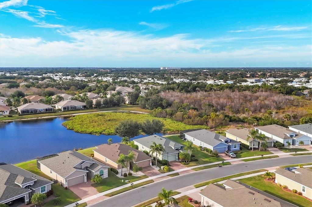 An aerial view shows a suburban neighborhood with houses bordering a lake and wooded area — 5283 CANYONLAND WAY, VENICE, FL
