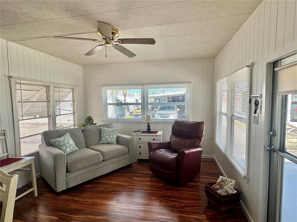 A sunroom with wood-look flooring, a gray sofa, a red recliner, and white paneled walls — 1501 25TH AVENUE DRIVE W, BRADENTON, FL