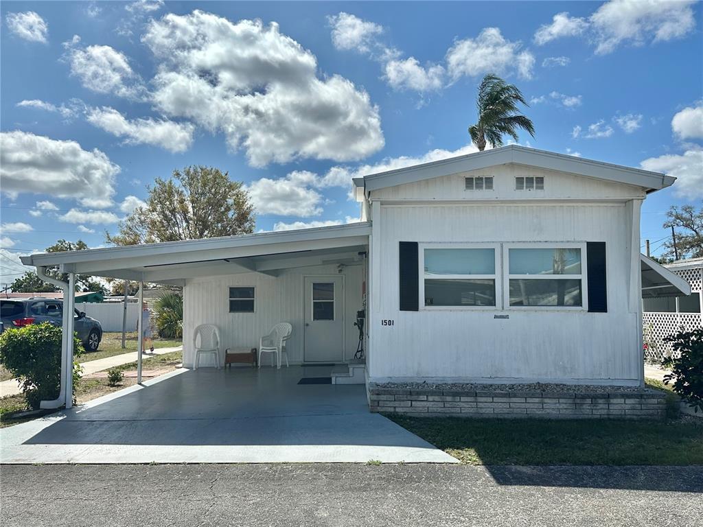 A white mobile home features a carport, a front entrance, and a brick-accented base — 1501 25TH AVENUE DRIVE W, BRADENTON, FL