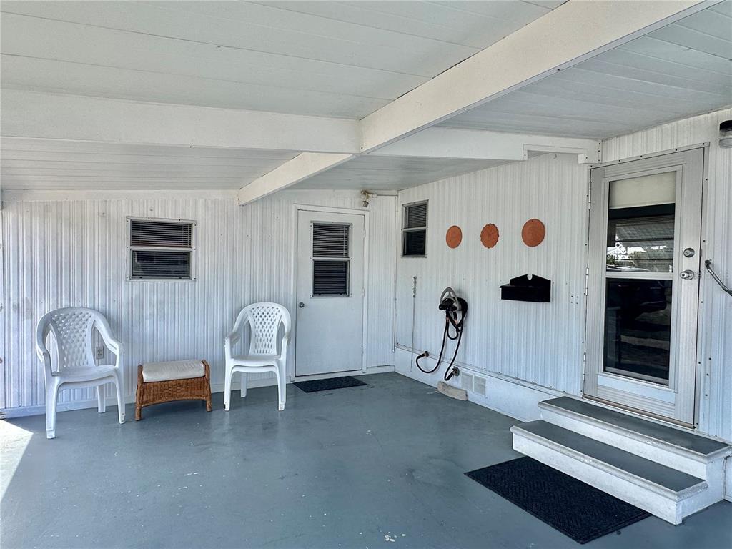 A covered porch features white siding, two white chairs, and two exterior doors — 1501 25TH AVENUE DRIVE W, BRADENTON, FL