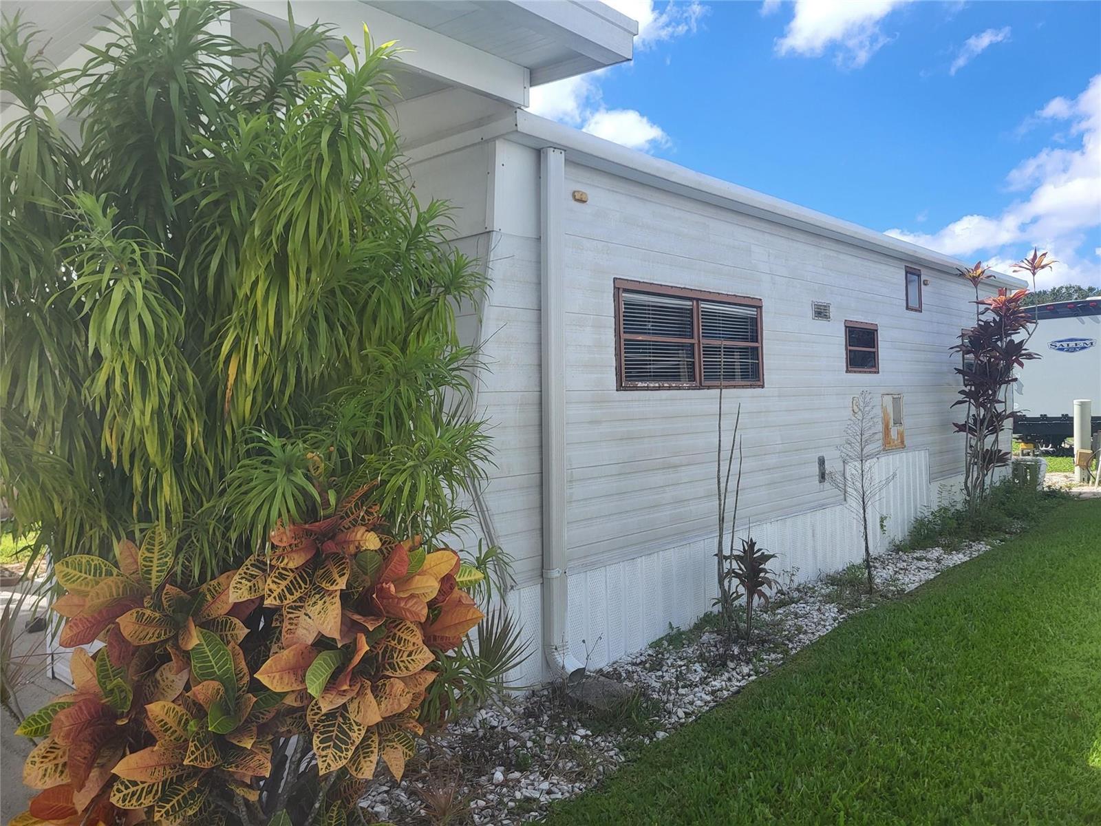 The exterior of a mobile home features light-colored siding, brown-framed windows, and decorative landscaping — 6502 SE 54th Lane, Okeechobee FL 34974, OKEECHOBEE, FL