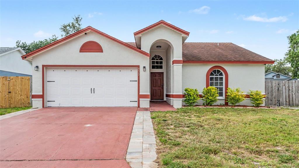 A single-story house with a white stucco exterior, red trim, and a two-car garage — 3312 QUEENS COVE LOOP, WINTER HAVEN, FL