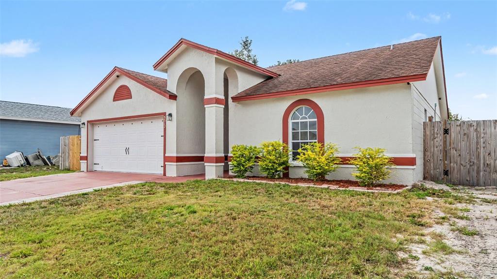 A single-story house with a white stucco facade, red trim, and an attached garage — 3312 QUEENS COVE LOOP, WINTER HAVEN, FL