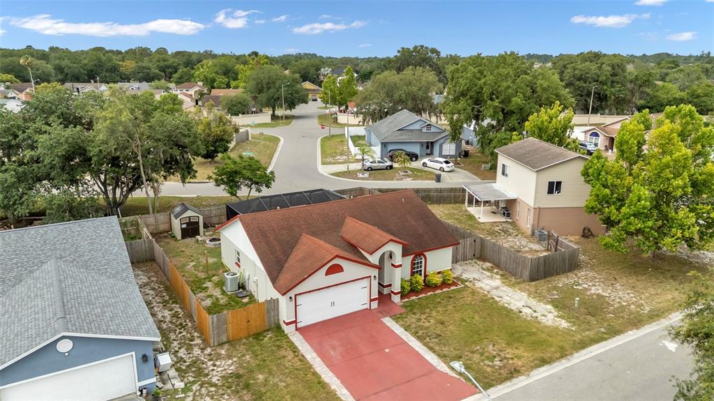 An aerial view shows a single-story house with a red roof and driveway in a neighborhood — 3312 QUEENS COVE LOOP, WINTER HAVEN, FL