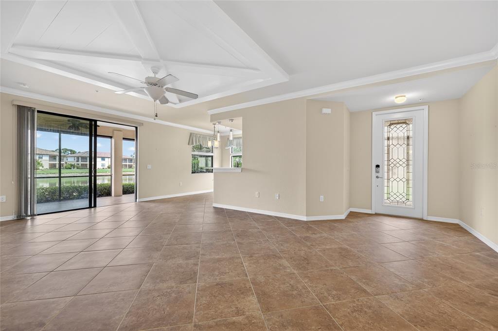 An open-concept living area features tan tile flooring, a coffered ceiling, and a glass-paneled door — 20151 RAGAZZA CIRCLE E UNIT 102, VENICE, FL