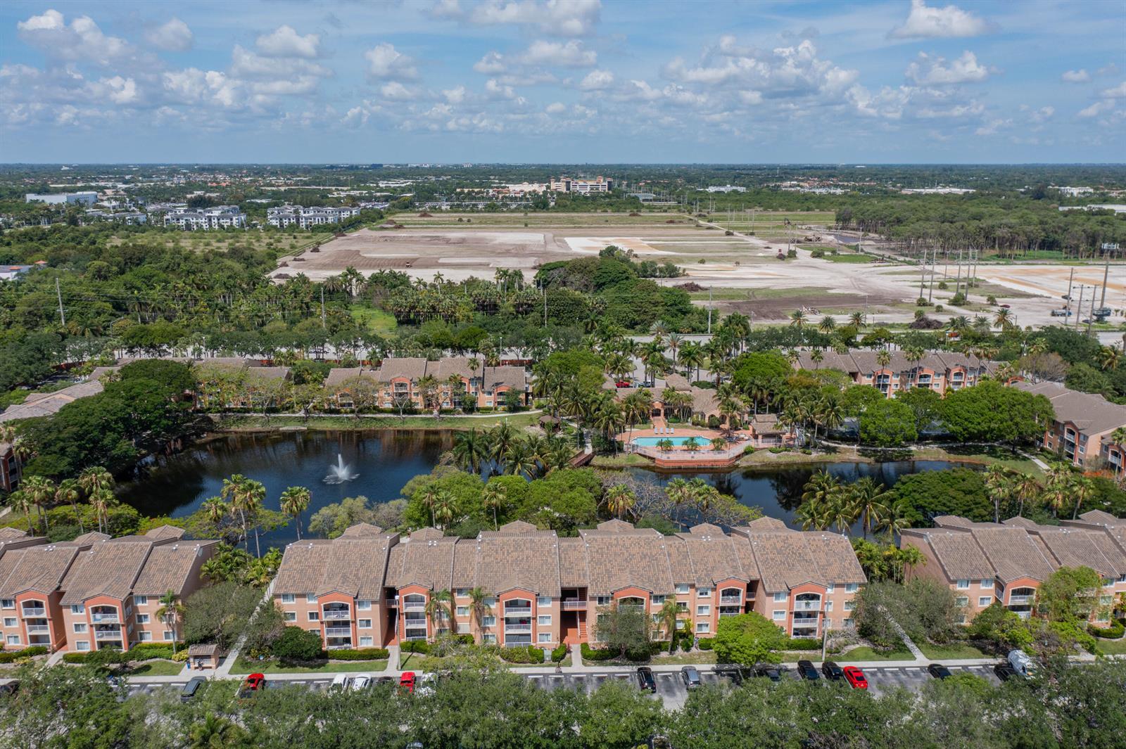 An aerial view shows a multi-story apartment complex surrounding a lake with a fountain — 3844 Lyons Road # 4, Coconut Creek FL 33073, COCONUT CREEK, FL