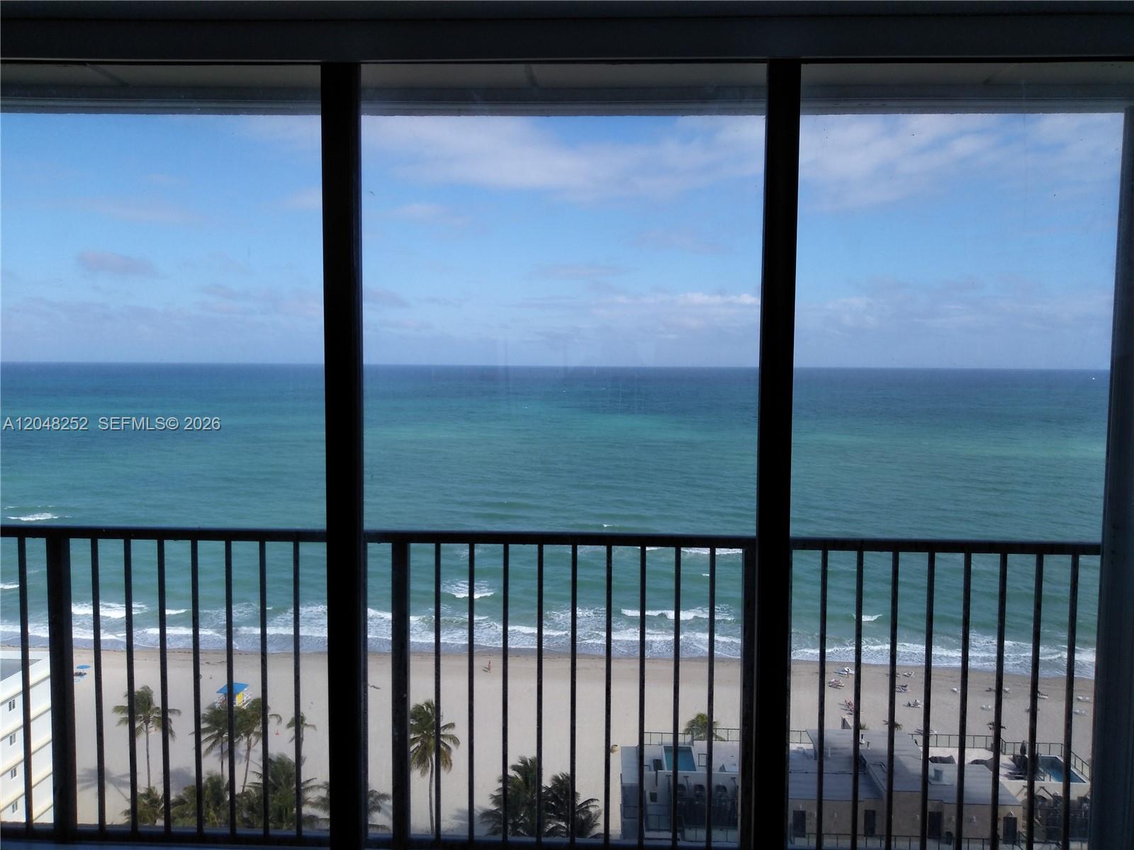 A view of the ocean and beach is seen through a large window with railings — 2101 S Ocean Dr # 2001, Hollywood FL 33019, HOLLYWOOD, FL