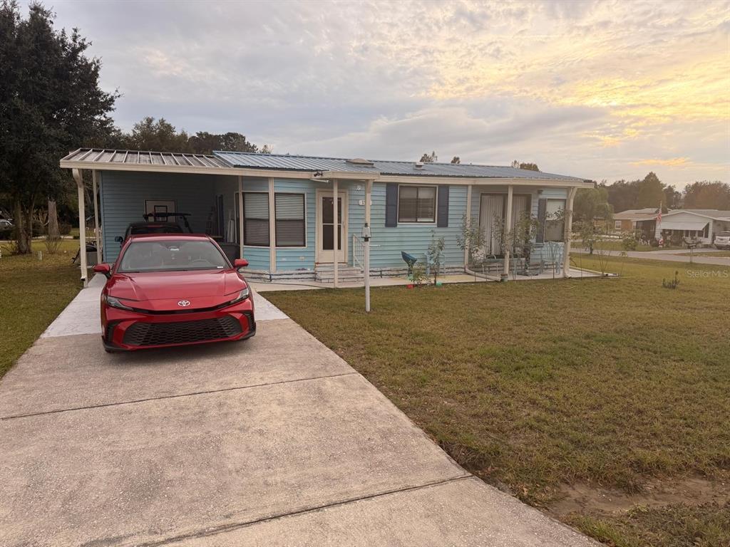 A light blue manufactured home with a metal roof, carport, and a red car parked outside — 121 HYDE PARK COURT, DAVENPORT, FL