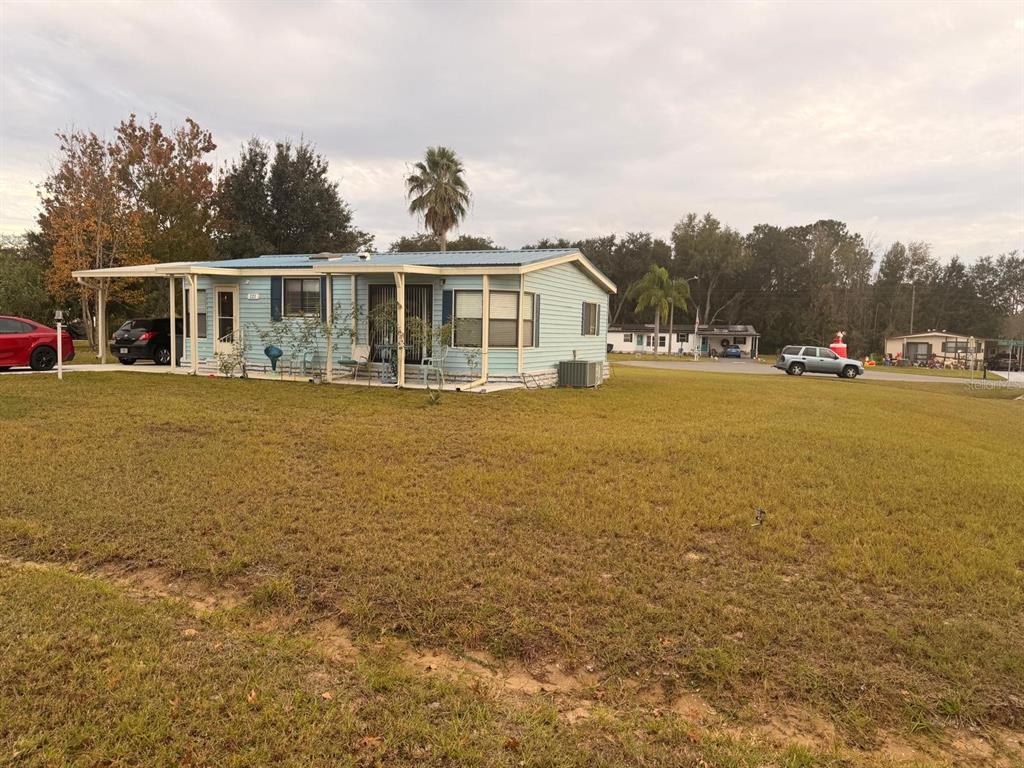 A light blue manufactured home with a metal roof and attached carport sits on grass — 121 HYDE PARK COURT, DAVENPORT, FL