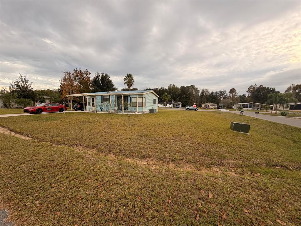 A light blue manufactured home sits on a large grass lot with a carport — 121 HYDE PARK COURT, DAVENPORT, FL