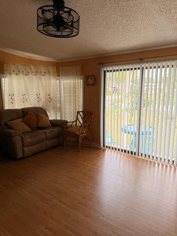 A living room features light wood-look flooring, a brown loveseat, a wicker chair, and vertical blinds — 121 HYDE PARK COURT, DAVENPORT, FL