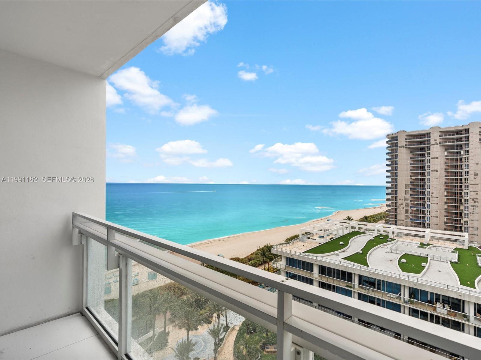 A balcony with a glass railing overlooks the ocean, beach, and nearby high-rise buildings — 6801 Collins Ave # 1208, Miami Beach FL 33141, MIAMI BEACH, FL