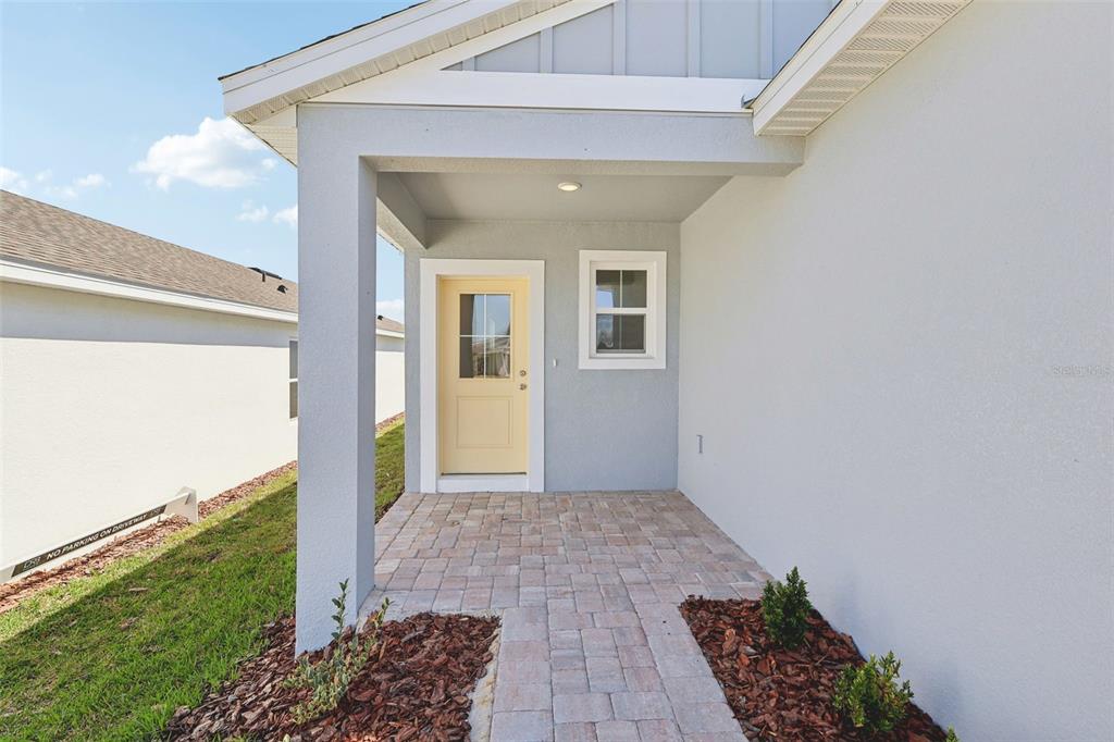 A light-colored house exterior features a covered entryway with a yellow door and pavers — 1929 DIAMOND HEAD CIRCLE, HAINES CITY, FL