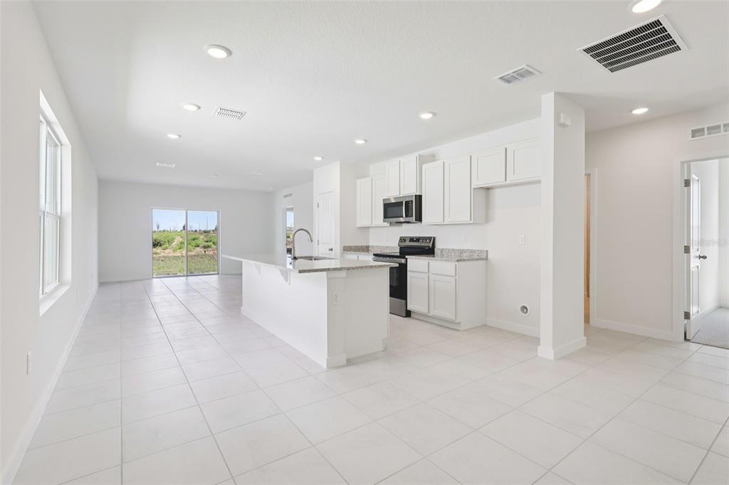 A bright kitchen with white cabinets, granite countertops, and tile flooring opens to a living area — 1929 DIAMOND HEAD CIRCLE, HAINES CITY, FL