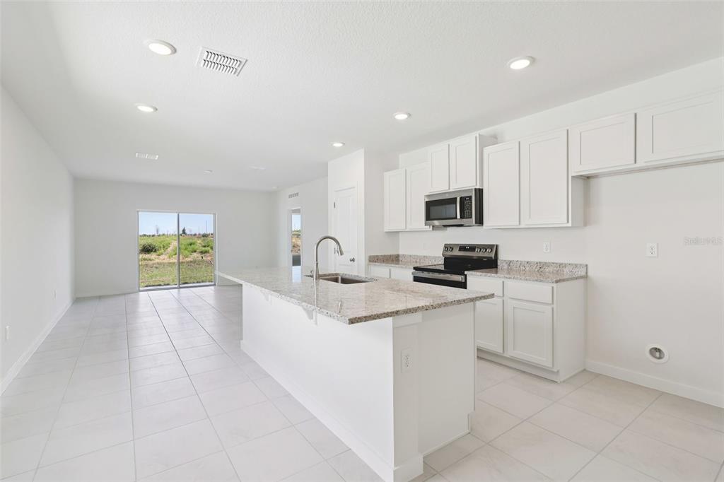 A bright kitchen features white cabinets, granite countertops, a center island, and tile flooring — 1929 DIAMOND HEAD CIRCLE, HAINES CITY, FL