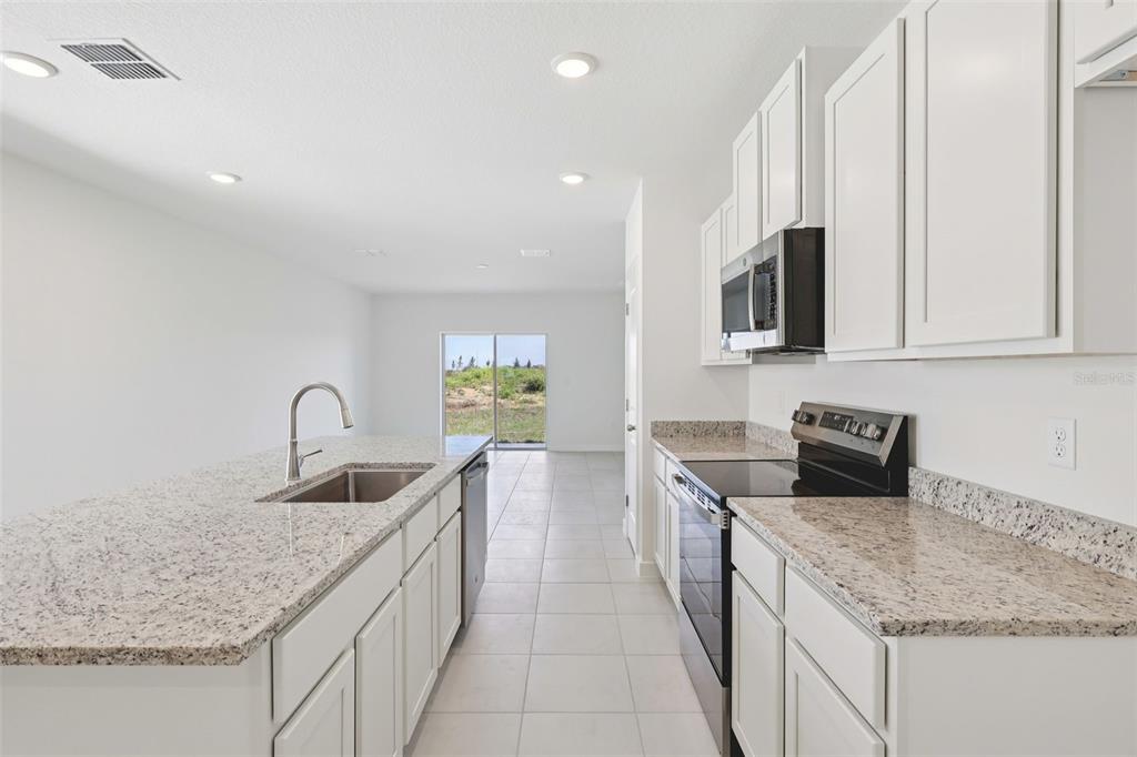 A modern kitchen features white cabinets, granite countertops, stainless steel appliances, and tile flooring — 1929 DIAMOND HEAD CIRCLE, HAINES CITY, FL