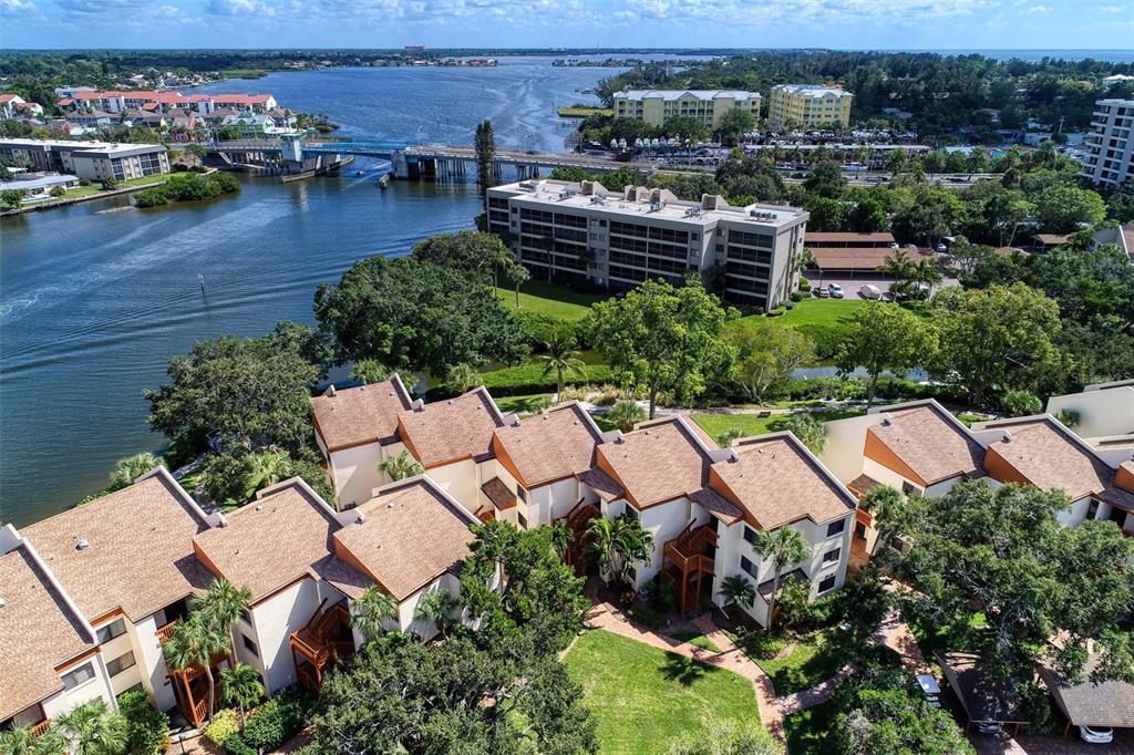 An aerial view shows multi-story residential buildings with brown roofs near a bridge and waterway — 1800 COVE II PLACE UNIT 213, SARASOTA, FL