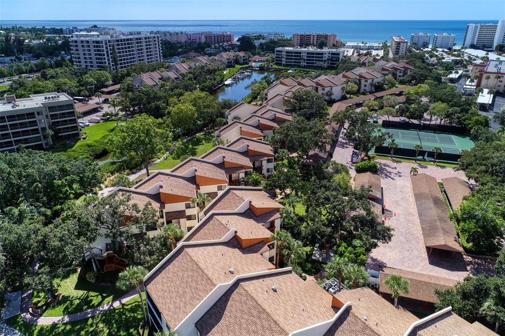 An aerial view shows a multi-story residential complex with brown roofs, tennis courts, and landscaping — 1800 COVE II PLACE UNIT 213, SARASOTA, FL