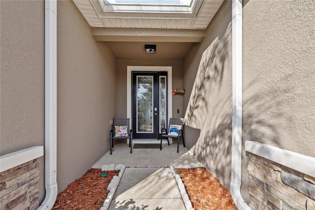 A covered entryway features a front door with glass panels, two chairs, and stone accents — 5453 SUNCATCHER DRIVE, WESLEY CHAPEL, FL