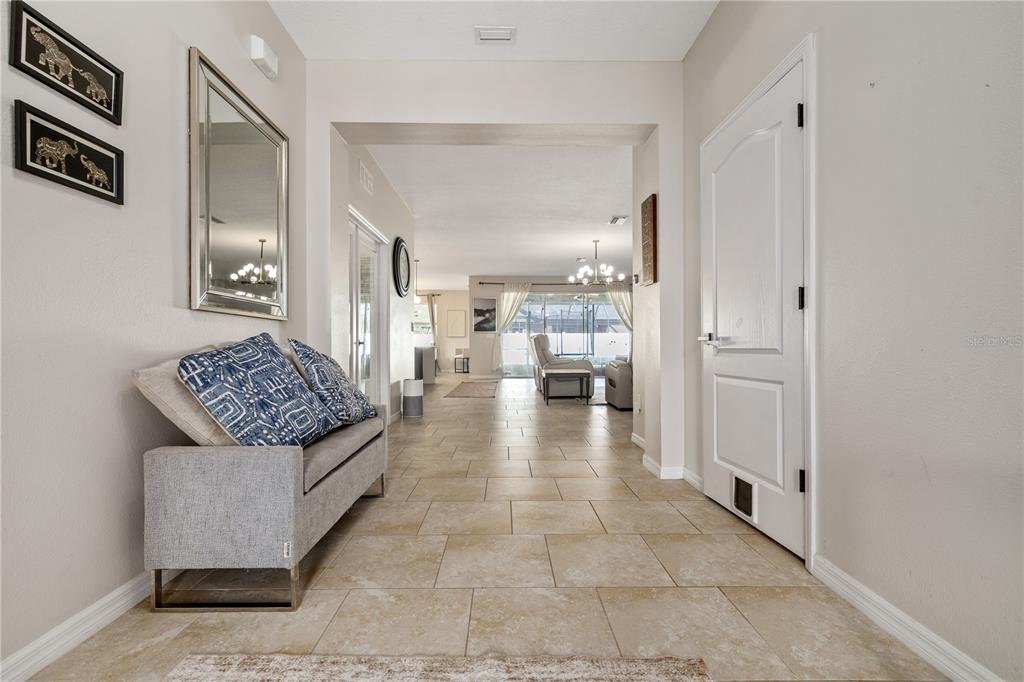 A tiled entryway features a gray bench, a wall mirror, and a view into the living area — 5453 SUNCATCHER DRIVE, WESLEY CHAPEL, FL