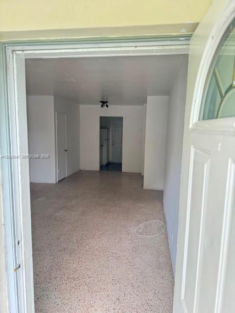 An interior view shows a room with speckled flooring leading to a doorway and hallway — NORTH MIAMI BEACH, FL