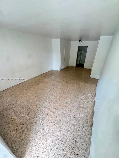 An empty room with white walls and speckled terrazzo flooring leads to a doorway — NORTH MIAMI BEACH, FL