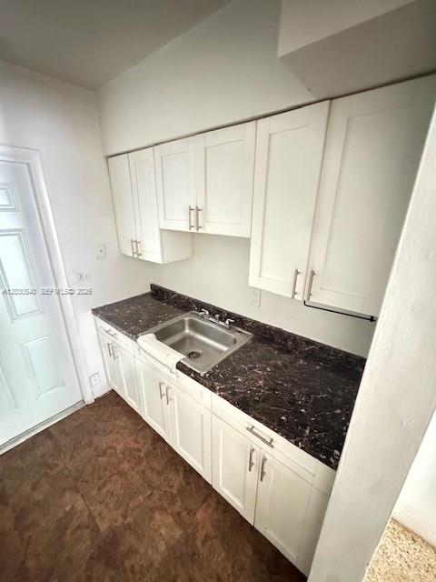 A kitchen features white cabinets, a dark countertop with a sink, and brown flooring — NORTH MIAMI BEACH, FL