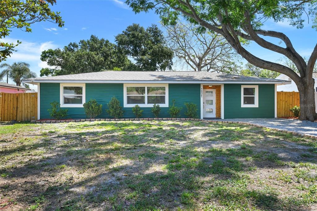 A single-story house with green horizontal siding, a white front door, and a gravel driveway — 1521 S JEFFERSON AVENUE, CLEARWATER, FL