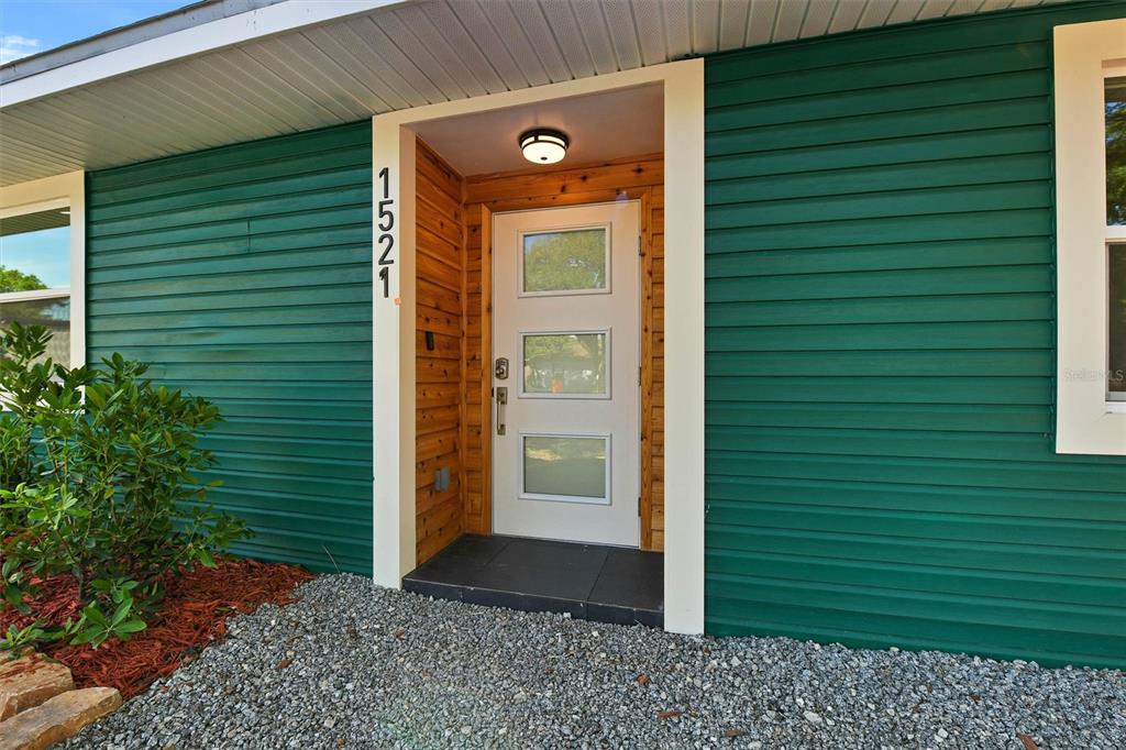 A white front door with three glass panels is set within a green-sided exterior wall — 1521 S JEFFERSON AVENUE, CLEARWATER, FL