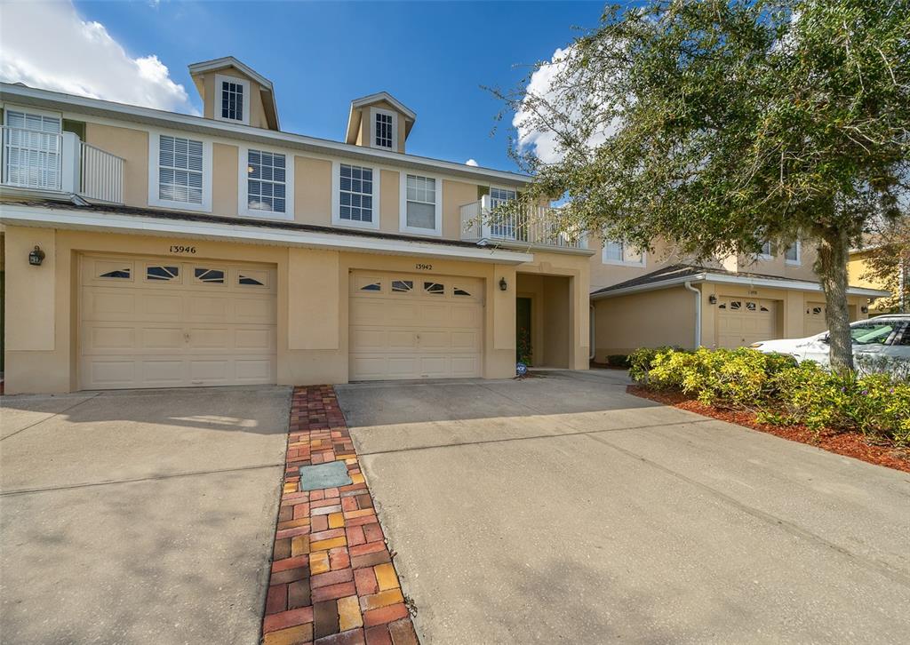A two-story townhouse exterior features beige stucco walls, two garage doors, and a brick walkway — 13942 DOVE WING COURT, ORLANDO, FL