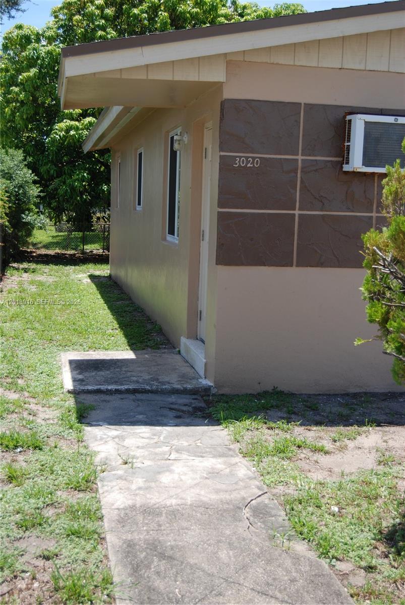 The exterior side of a tan house features a stone walkway and a window unit — 3020 NW 71st St, Miami FL 33147, MIAMI, FL