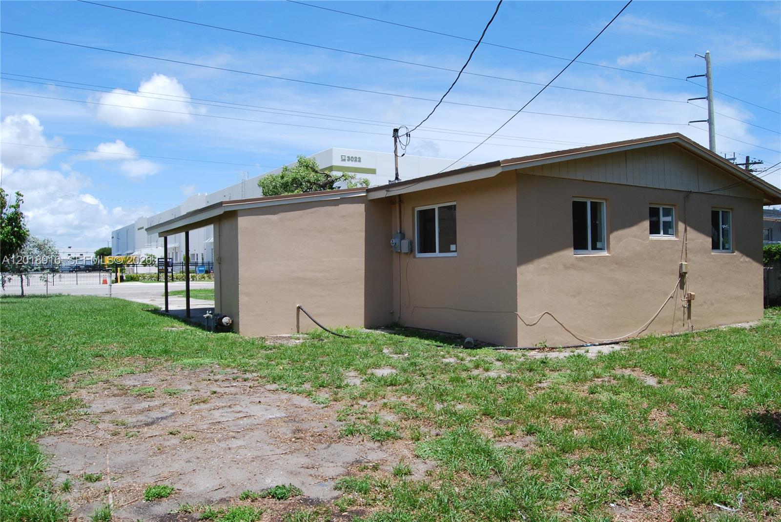 The exterior of a tan, single-story house features a small covered patio and a grassy yard — 3020 NW 71st St, Miami FL 33147, MIAMI, FL