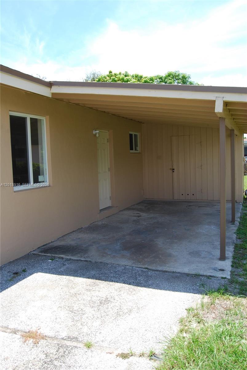 A tan house exterior features a concrete carport, a white door, and a small window — 3020 NW 71st St, Miami FL 33147, MIAMI, FL