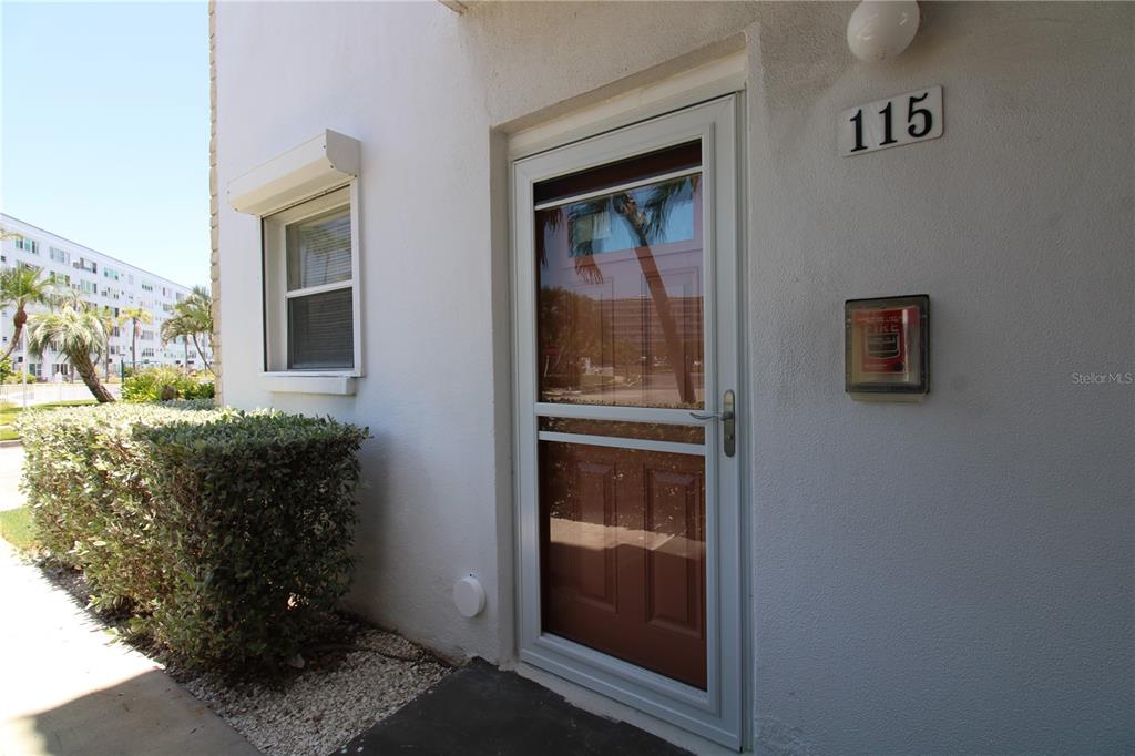 The exterior view shows a white building entrance with a storm door and unit number 115 — 3128 59TH STREET S UNIT 115, GULFPORT, FL