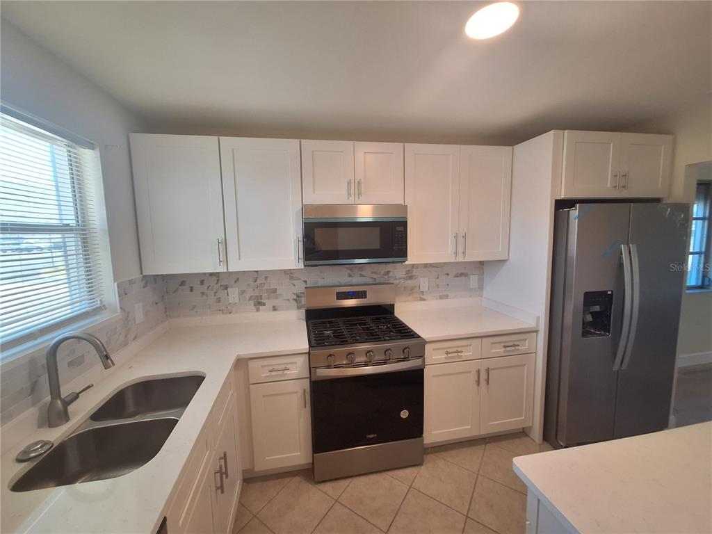 A kitchen features white cabinets, stainless steel appliances, a tiled backsplash, and light countertops — 3128 59TH STREET S UNIT 115, GULFPORT, FL