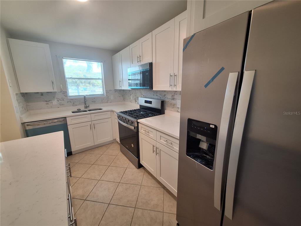 A kitchen features white cabinets, stainless steel appliances, a tiled backsplash, and light-colored countertops — 3128 59TH STREET S UNIT 115, GULFPORT, FL