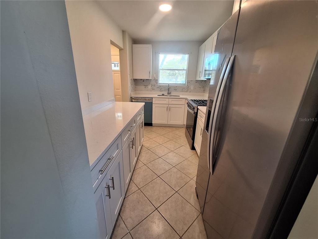 A kitchen features white cabinetry, stainless steel appliances, quartz countertops, and diagonal tile flooring — 3128 59TH STREET S UNIT 115, GULFPORT, FL