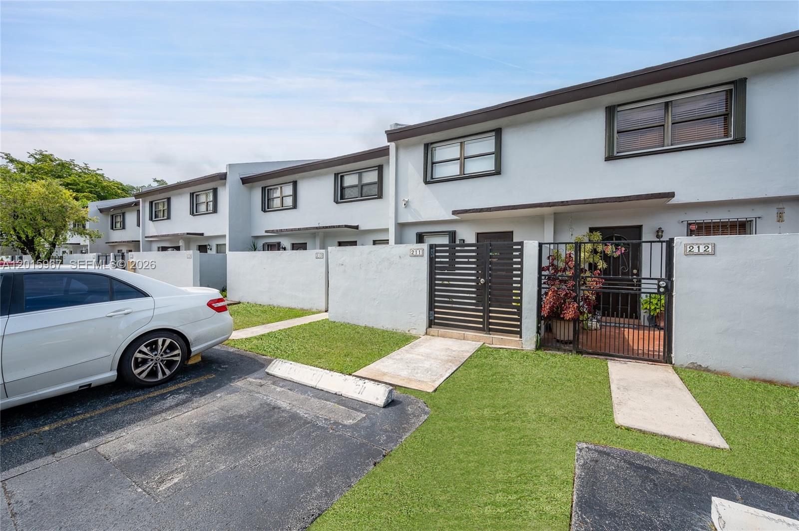 A row of two-story townhouses with white stucco walls, private gated courtyards, and parking spaces — 8010 SW 152nd Ave # 211, Miami FL 33193, MIAMI, FL