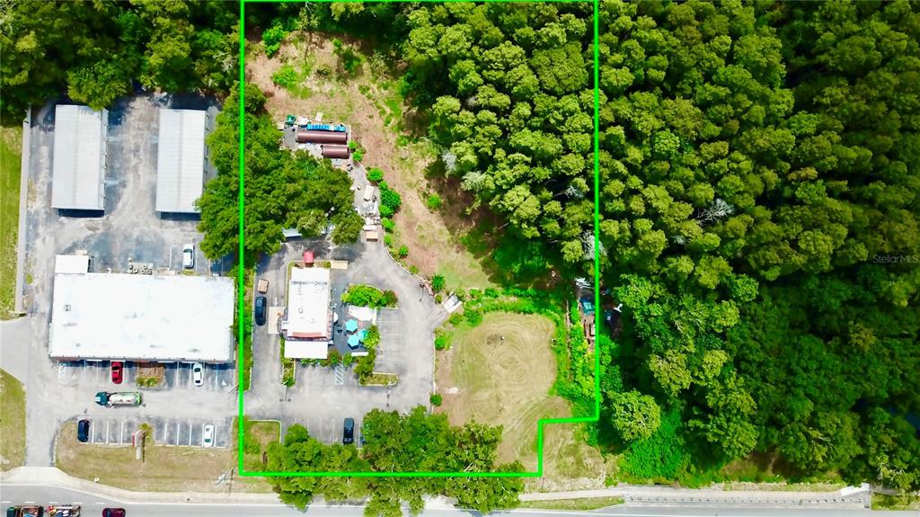 An aerial view shows a commercial property with buildings, parking, and surrounding wooded land — 2318 SEVEN SPRINGS BOULEVARD, NEW PORT RICHEY, FL