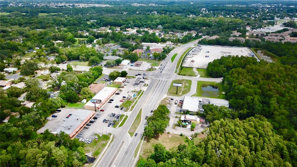 An aerial view shows a commercial intersection with parking lots, buildings, and surrounding wooded areas — 2318 SEVEN SPRINGS BOULEVARD, NEW PORT RICHEY, FL