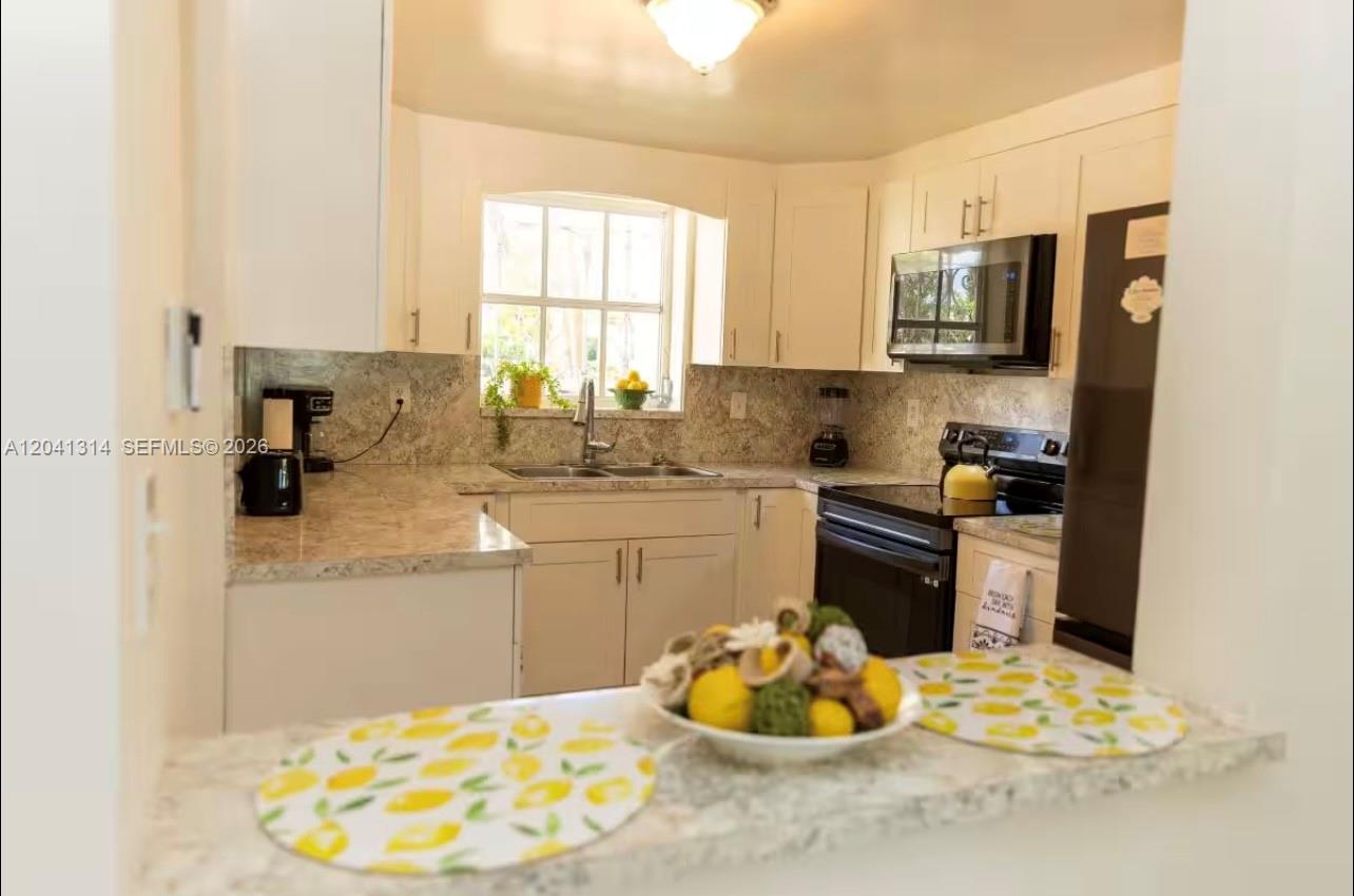 A kitchen features white cabinets, granite countertops, a window, and a breakfast bar — 1949 NE 123rd St # 0, North Miami FL 33181, NORTH MIAMI, FL