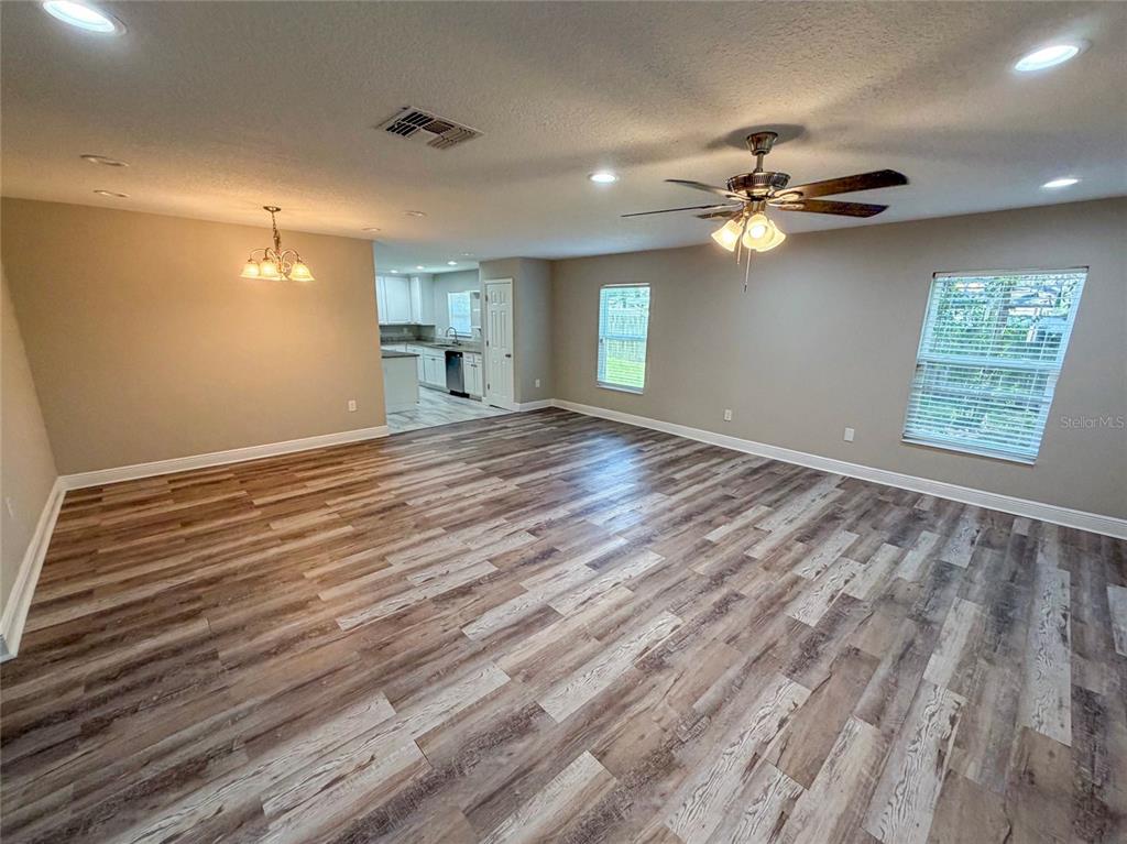 A spacious room with wood-look flooring, a ceiling fan, and an adjacent kitchen area — 312 WADE AVENUE, DELAND, FL