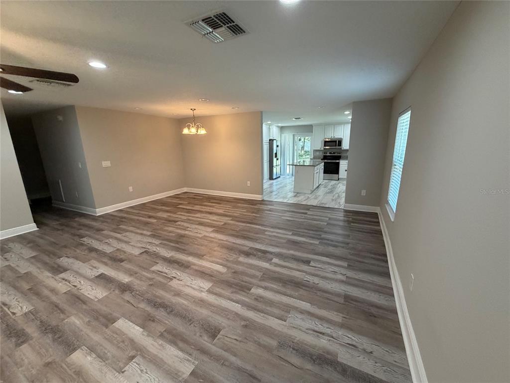 An open-concept living and dining area features wood-look flooring and a view into the kitchen — 312 WADE AVENUE, DELAND, FL