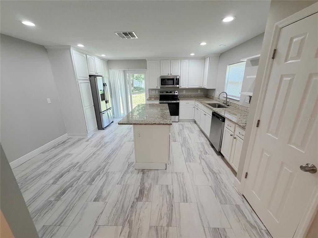A kitchen features white cabinets, granite countertops, a center island, and light-colored wood-look tile flooring — 312 WADE AVENUE, DELAND, FL