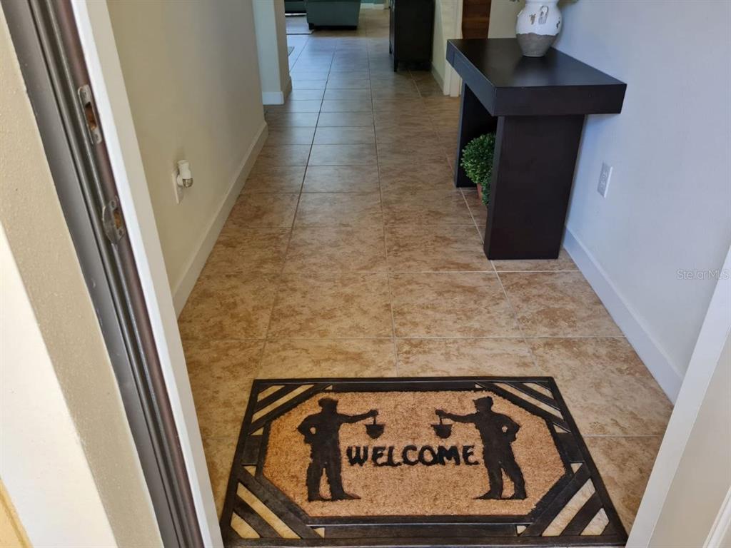 An entryway features a welcome mat on tan tile flooring leading to a dark console table — 8923 CUBAN PALM ROAD, KISSIMMEE, FL
