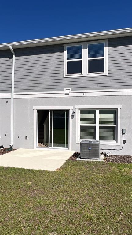 The exterior rear view of a two-story home features a concrete patio and sliding door — 9324 WESTSIDE HILLS DRIVE, DAVENPORT, FL