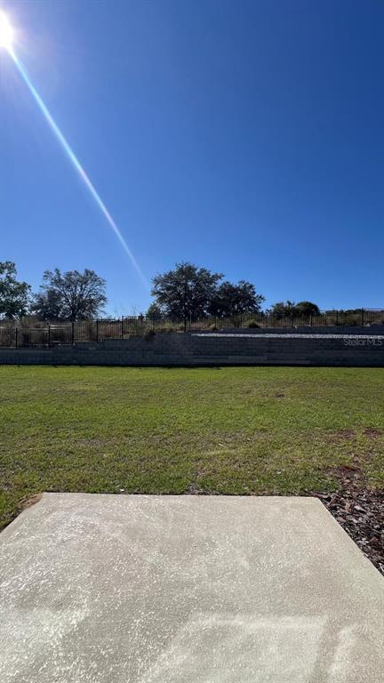 A concrete patio overlooks a grassy backyard with a tiered stone retaining wall and fence — 9324 WESTSIDE HILLS DRIVE, DAVENPORT, FL