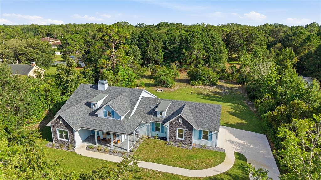 An aerial view shows a light blue house with a gray roof and stone accents — 26644 EASY STREET, WESLEY CHAPEL, FL