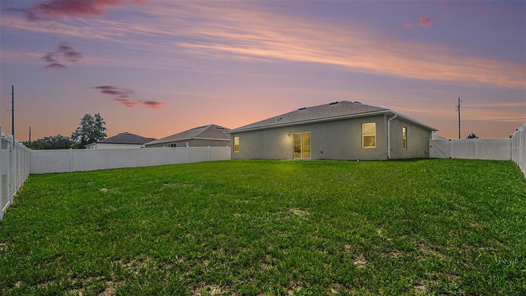 The exterior rear view of a single-story house with a fenced-in grassy backyard at sunset — 13537 SW 47TH CIRCLE, OCALA, FL