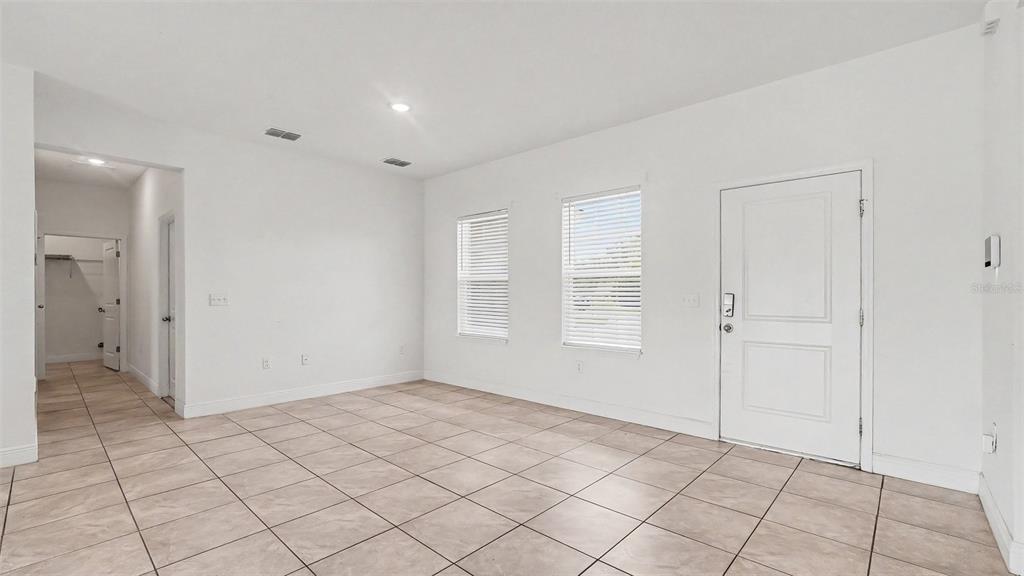 A bright, empty room features white walls, tiled flooring, two windows, and a white door — 13537 SW 47TH CIRCLE, OCALA, FL
